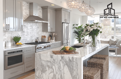 Residential Renovation Epping featuring a modern kitchen with a marble island benchtop, custom grey cabinetry, stainless steel appliances, pendant lighting, and a bright open-plan living area by East West Homes Builder.